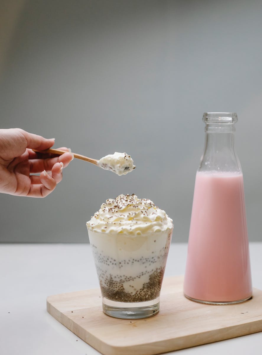 A glass of chia seed pudding topped with whipped cream next to a pink milk bottle.