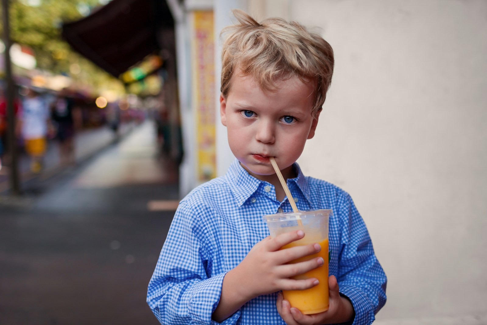 A young boy in a blue shirt drinks orange juice
